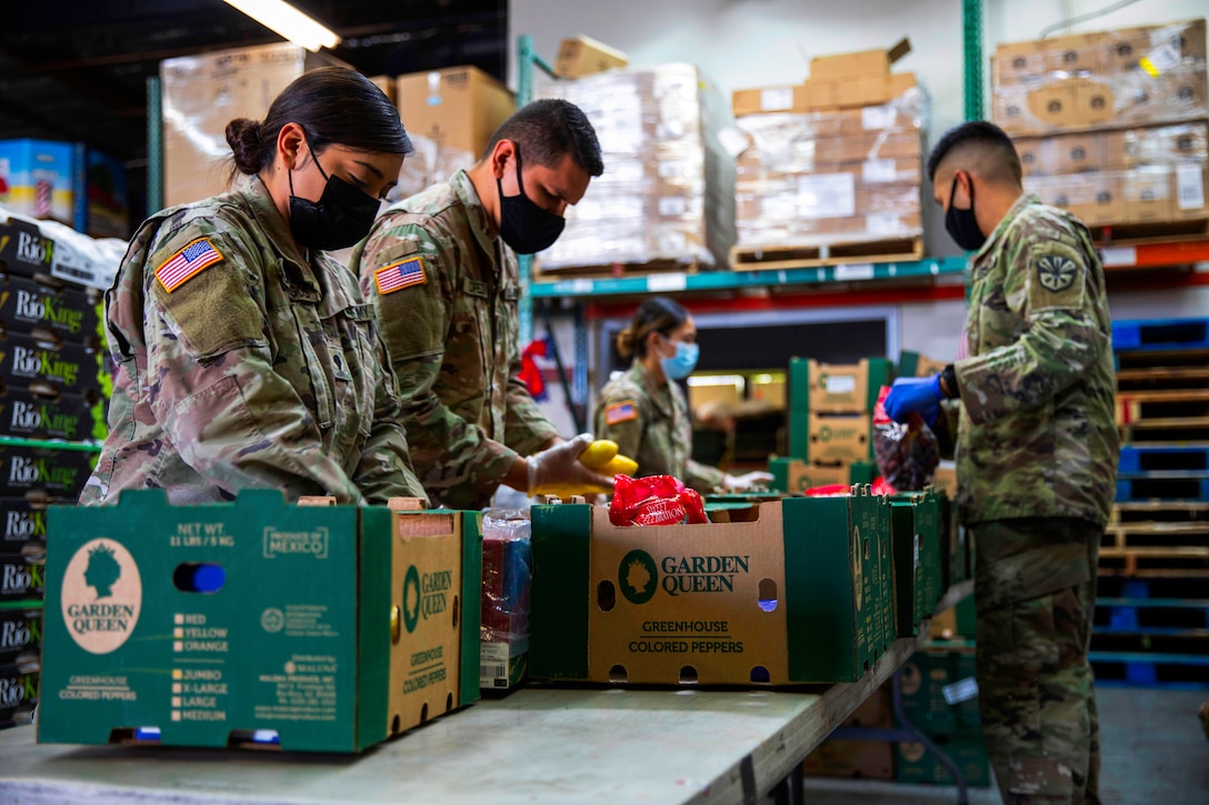 Soldiers wearing face masks and gloves fill boxes with fresh produce at a local food bank.