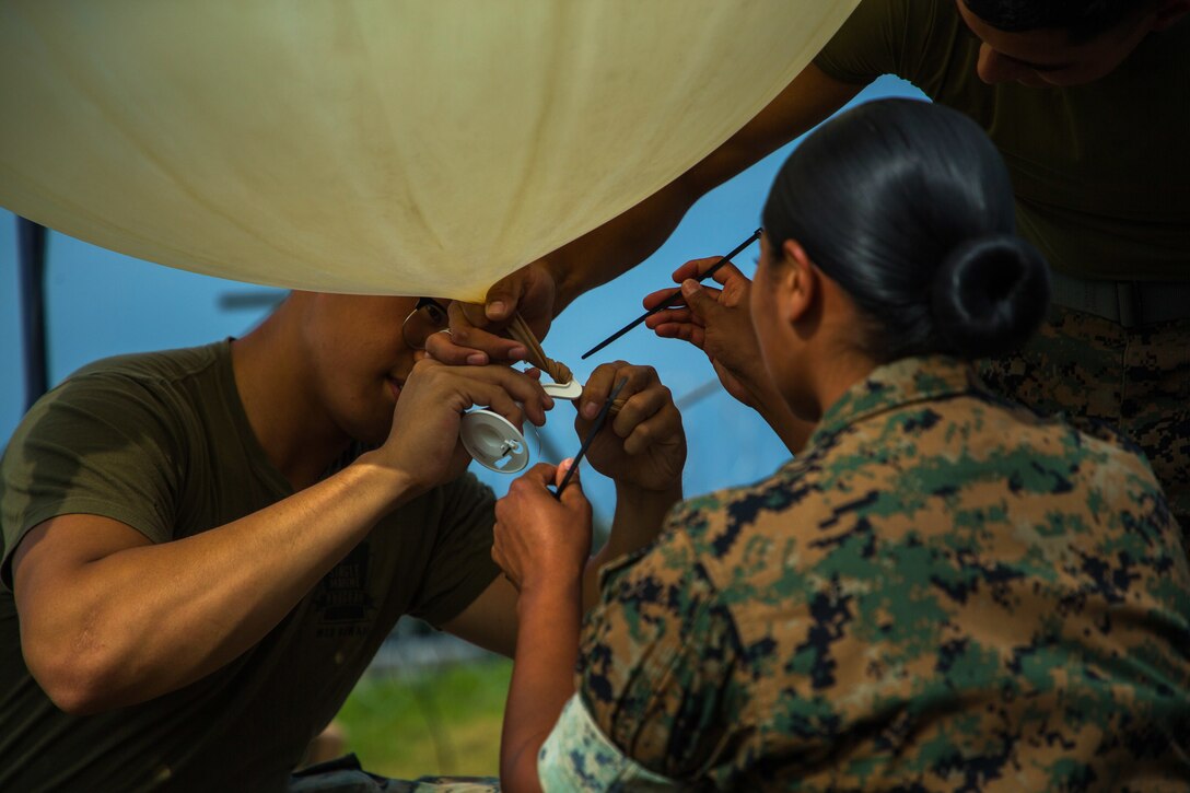 Three Marines prepare a weather balloon for flight.