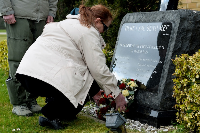 A woman bends down to put flowers in front of a large plaque.