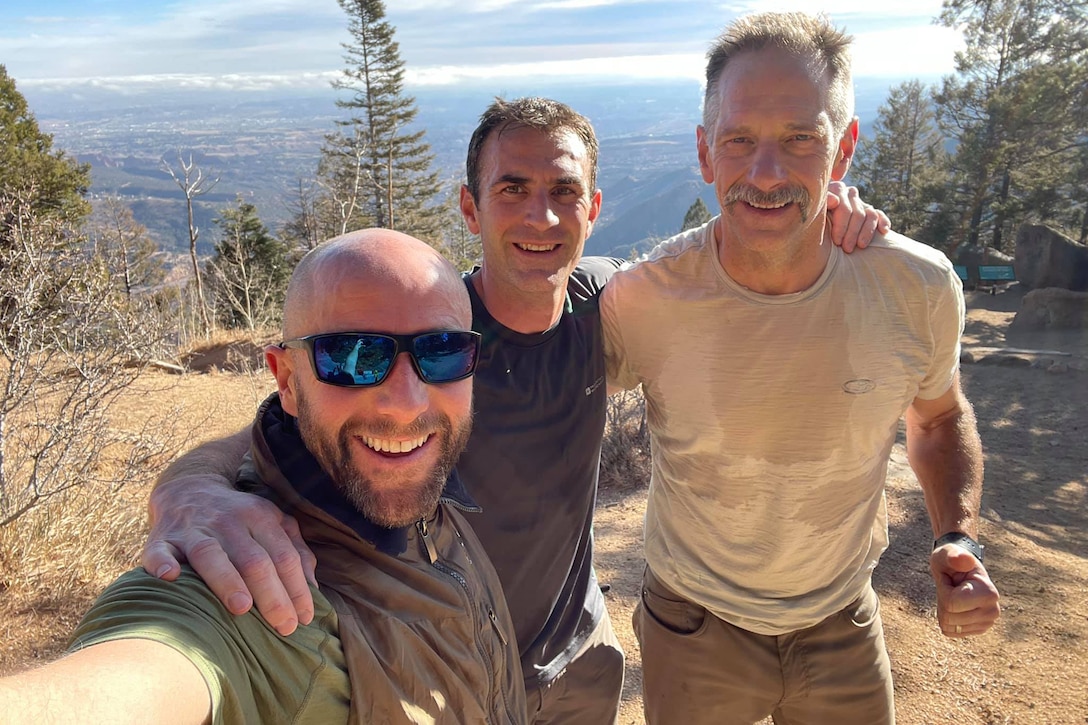 Three men embrace for a photo on a mountainside.