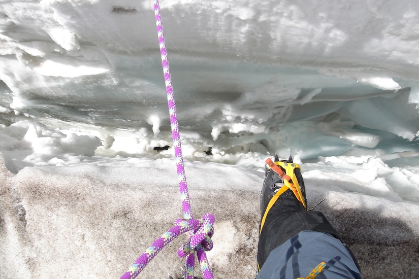 A rope and a boot sit near the edge of a snowy crevasse.