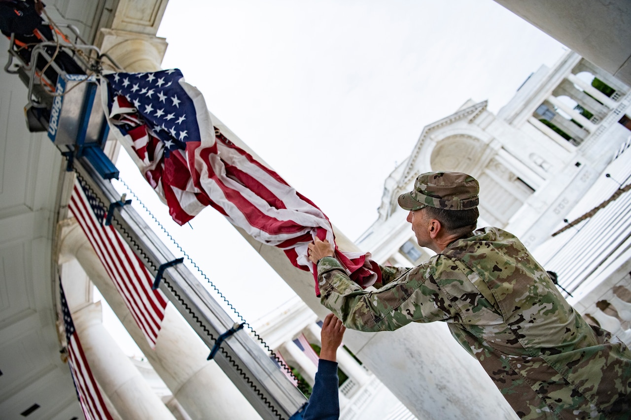 A service member hangs a flag on a building.
