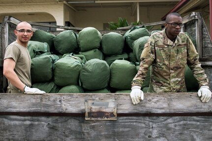 Two Airmen with a truck full of duffle bags.