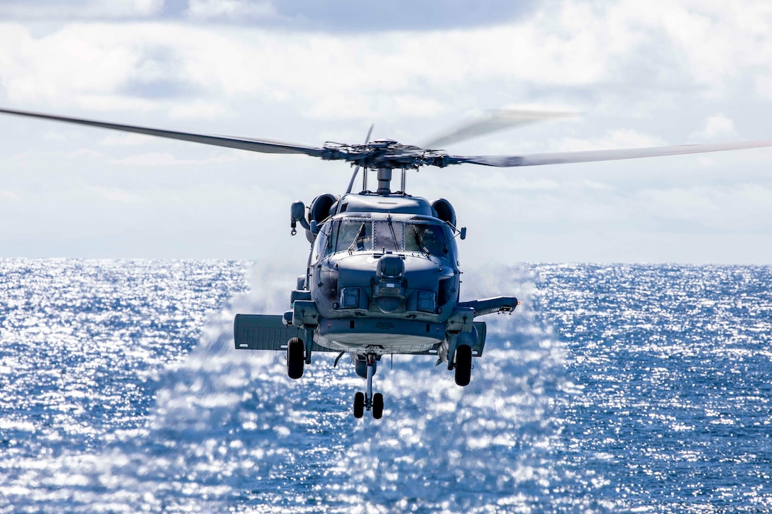 A Navy helicopter flies over water.
