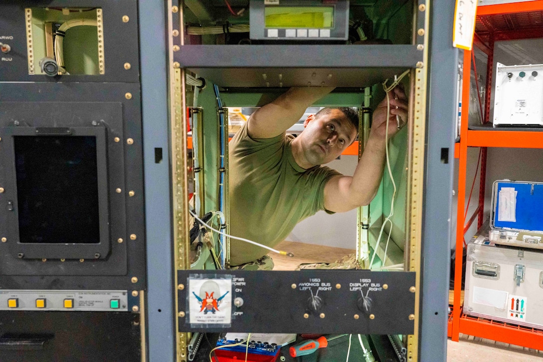 An airman adjusts wires on a piece of equipment.