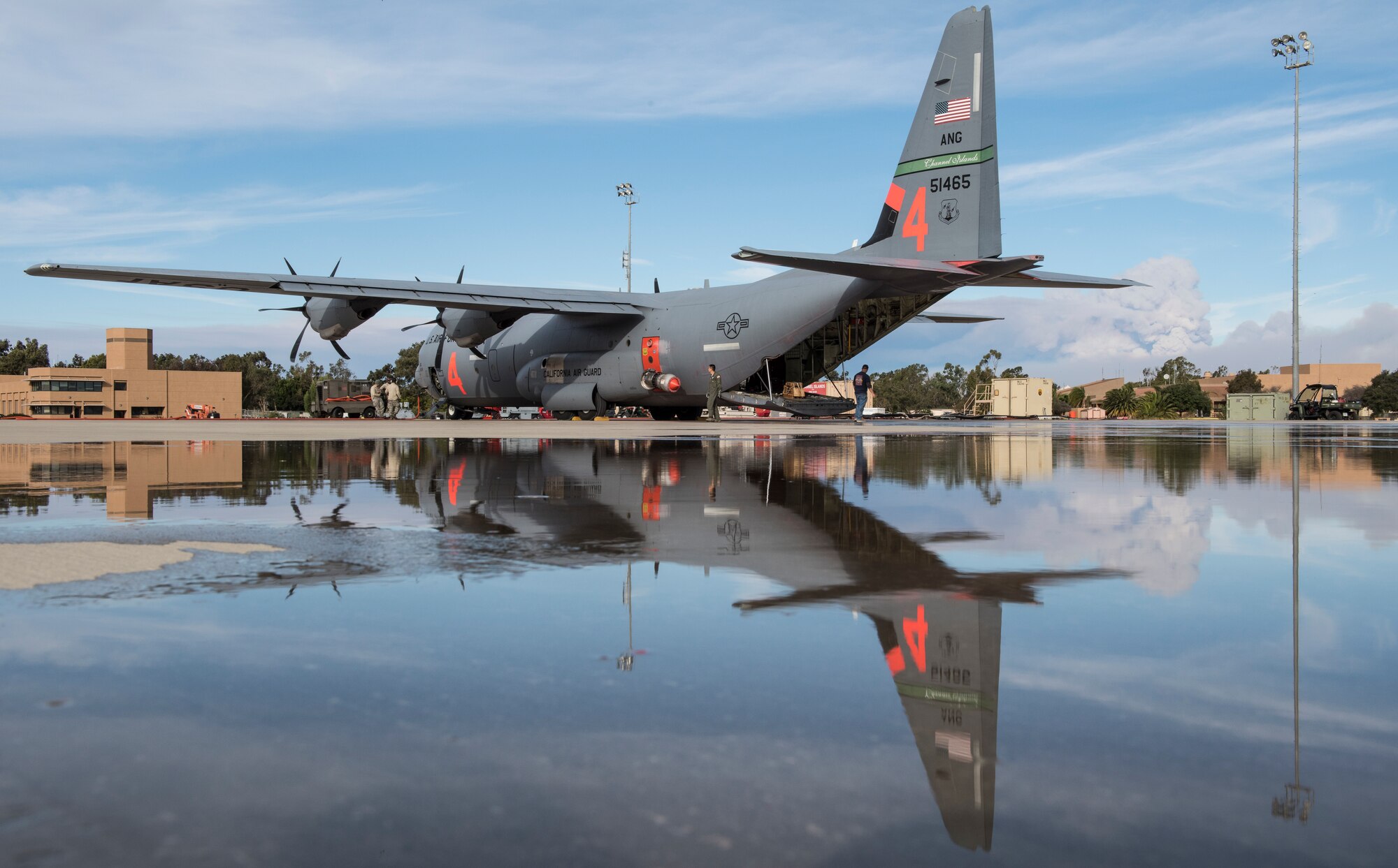 A C-130J Hercules from the 146th Airlift Wing, California Air National Guard, sits on the flightline at Channel Islands Air National Guard Station as the Thomas Fire burn in the background, Dec. 10, 2017. The 146th was activated to support CAL FIRE with wildfire suppression efforts within the state. The C-130s here are capable of spraying fire retardant from a modular airborne firefighting systems loaded in the cargo bay. (U.S. Air Force photo/Master Sgt. Brian Ferguson)