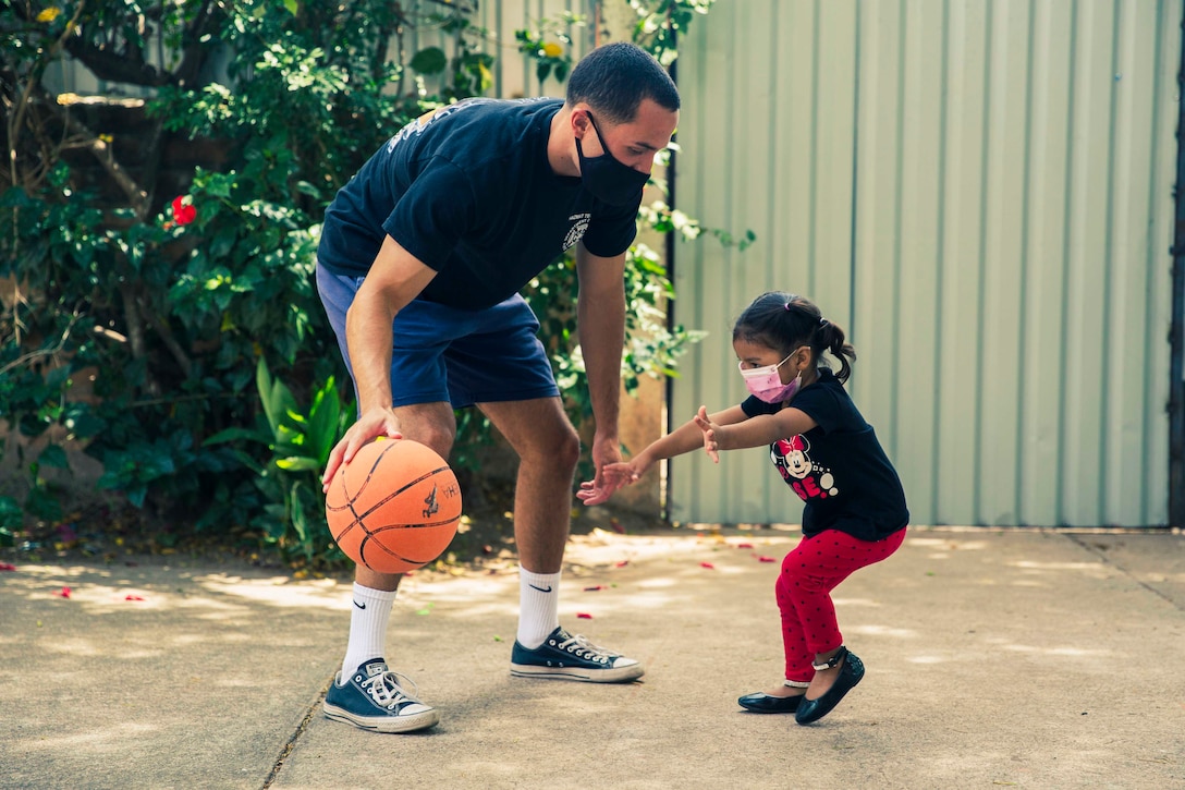 An airman plays basketball with a young child.