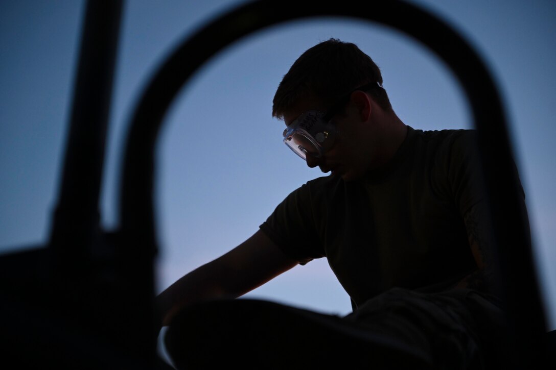 An airman shown in silhouette checks the engine of an aircraft.