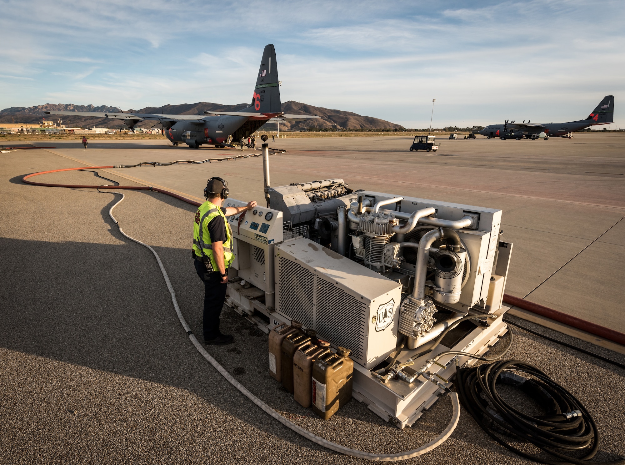 A fuels technician runs a pump fueling a C-130J of the 146th Airlift Wing on the flightline at Channel Islands Air National Guard Base in Port Hueneme, California, Dec. 9, 2017. It takes just 15-20 minutes to pump a mixture of dry chemicals and water into the storage tank of the MAFFS unit, which is loaded in the cargo bay, and launch the aircraft on another fire-fighting sortie. (U.S. Air Force photo by J.M. Eddins Jr.)