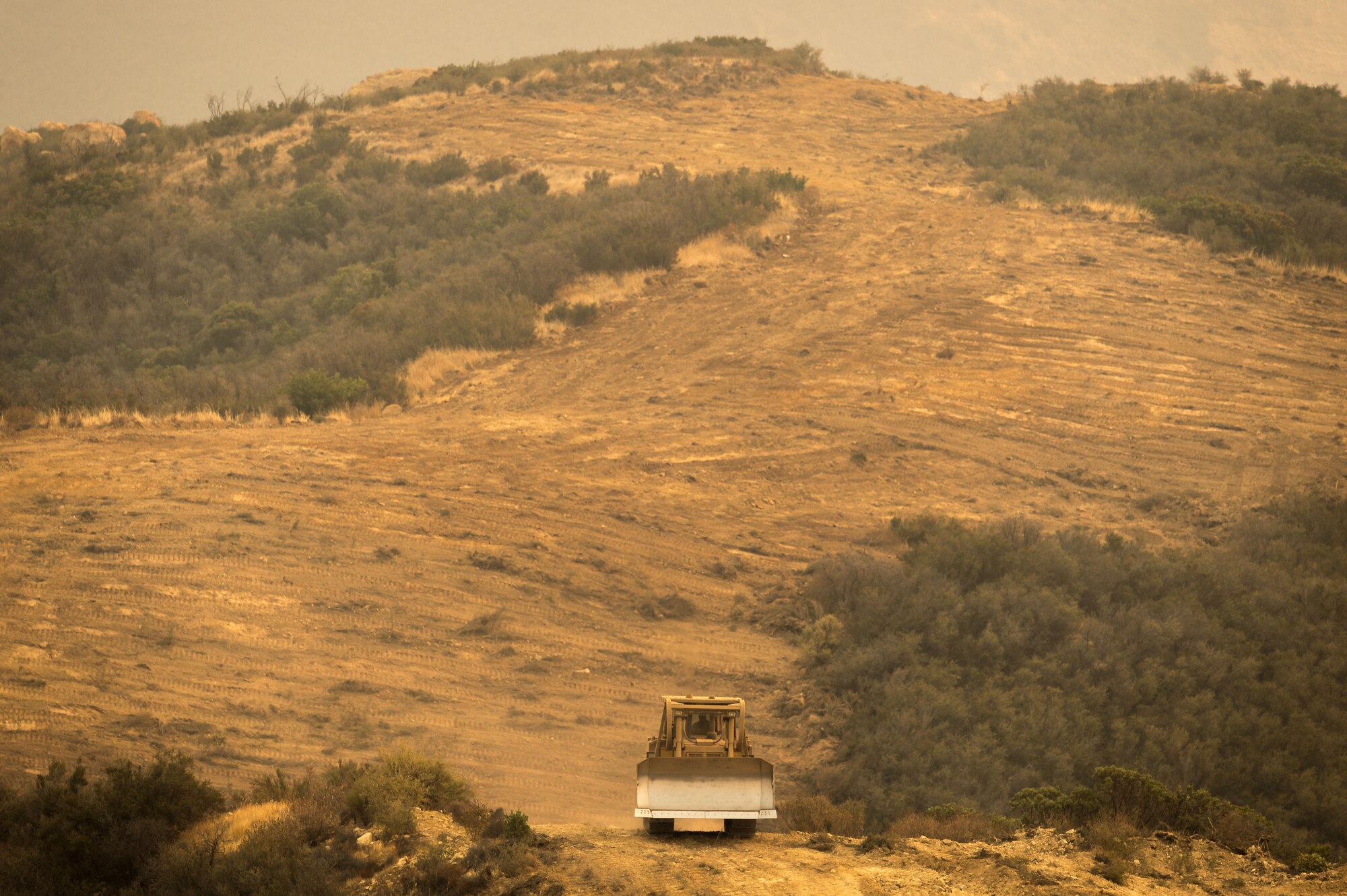 A bulldozer clears away foliage to form a fire-break on a ridge in the Los Padres National Forest above Santa Barbara, California, Dec. 11, 2017. C-130Js of the 146th Airlift Wing later dropped fire retardant chemicals along these fire-breaks to further slow the advance of the Thomas Fire, a large wildfire burning through Ventura and Santa Barbara Counties. (U.S. Air Force photo by J.M. Eddins Jr.)