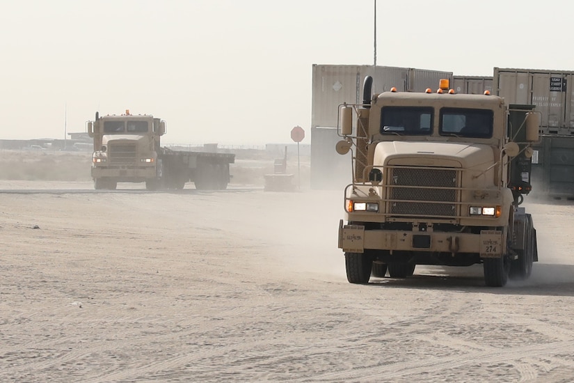 Two trucks move across a dusty field.
