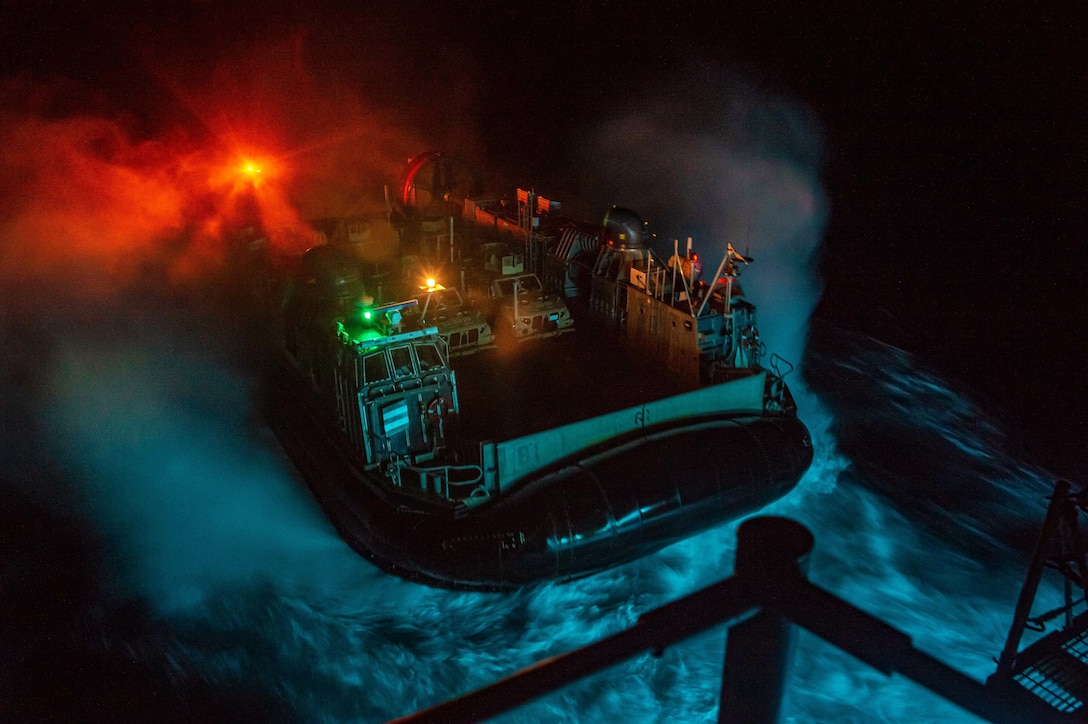 A water craft approaches a ship in the ocean at night.