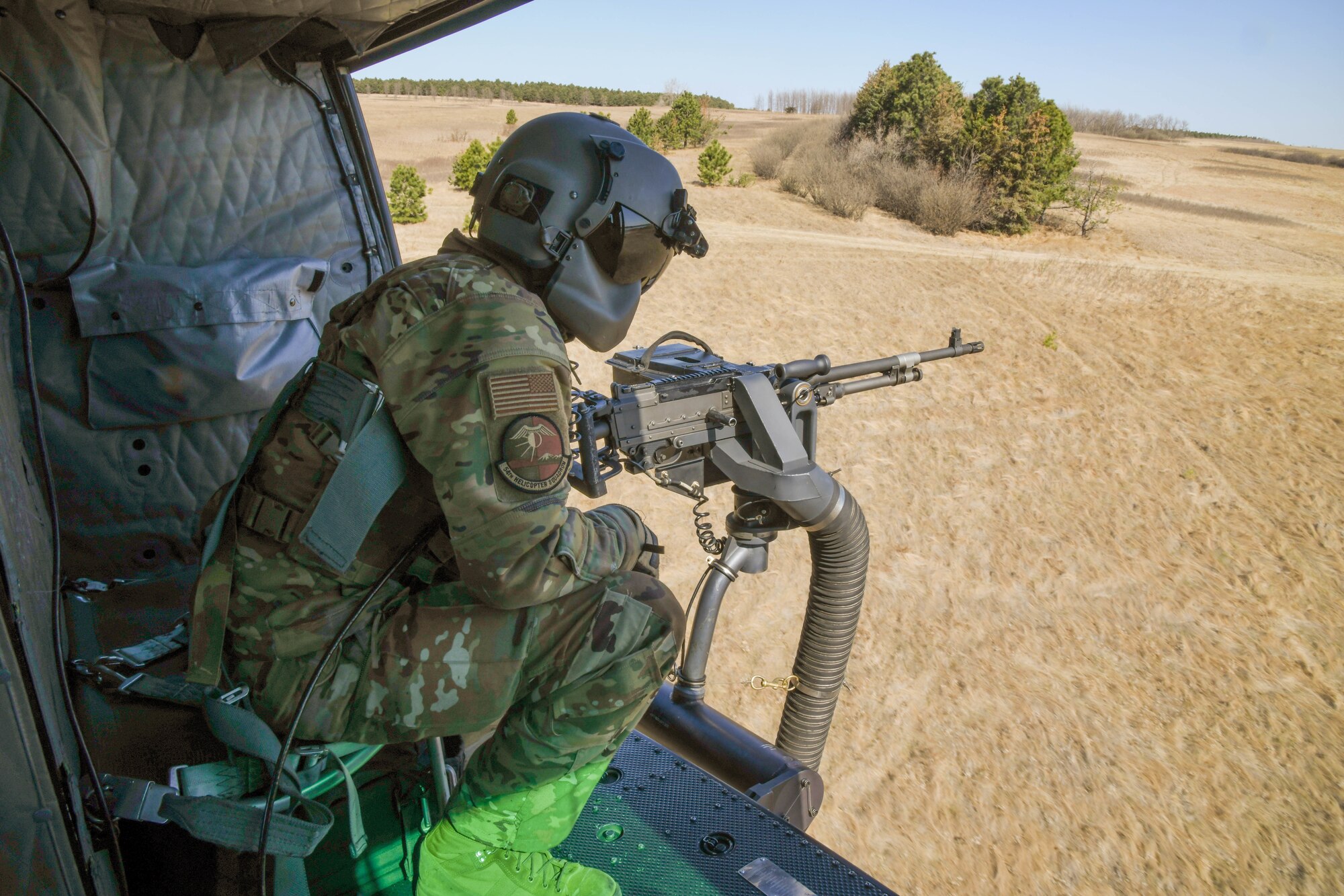 an Airman mans a gun inside of a flying helicopter