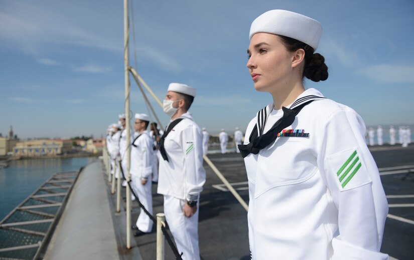 Sailors stand along the edge of an aircraft carrier as it returns to port.