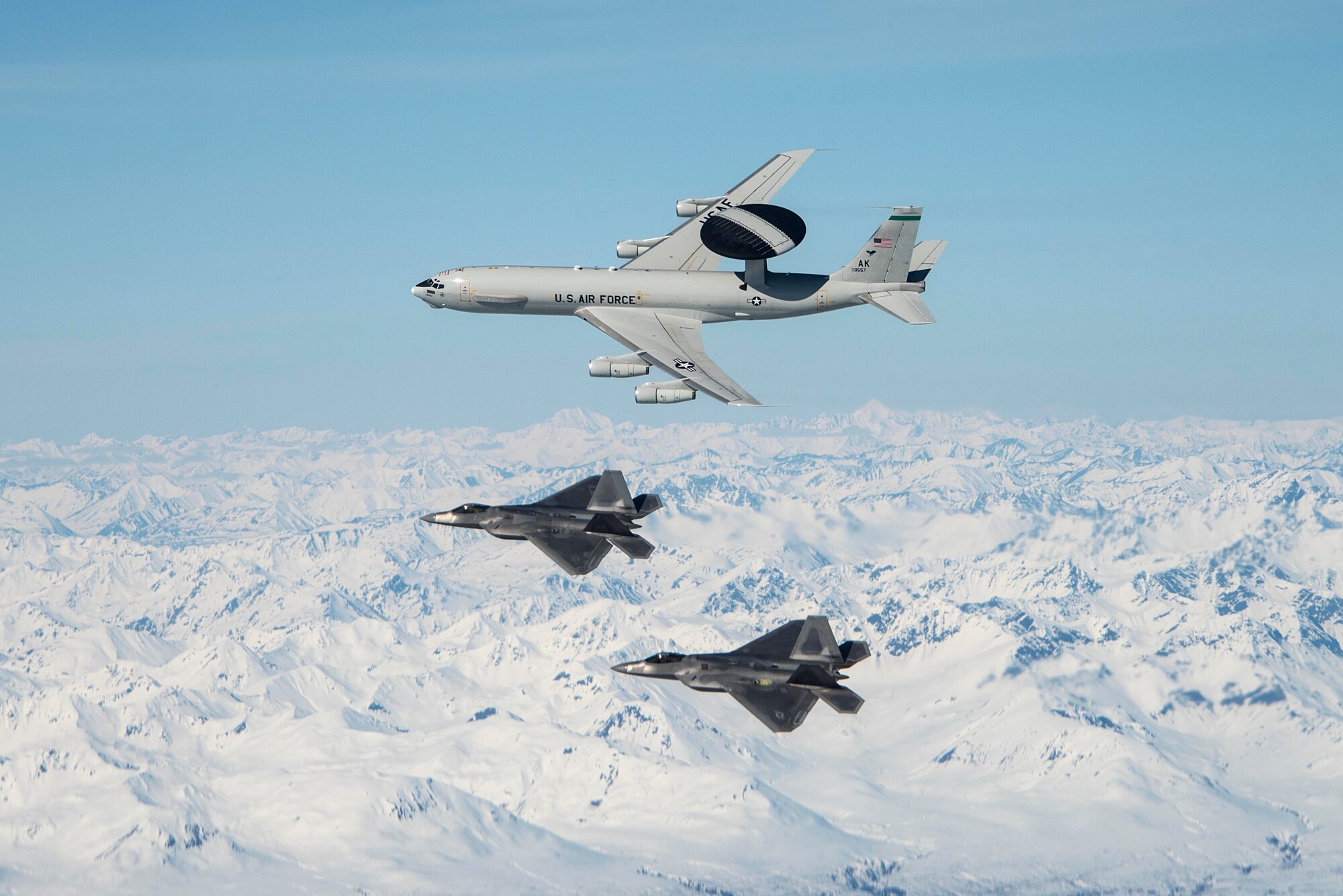 An E-3 Sentry and F-22 Raptors assigned to Joint Base Elmendorf-Richardson, Alaska, fly over mountains May 5, 2020. The aircraft were part of a formation flight demonstrating airpower and consisted of active duty, Guard and Reserve components. (U.S. Air Force photo by Tech. Sgt. Jerilyn Quintanilla)