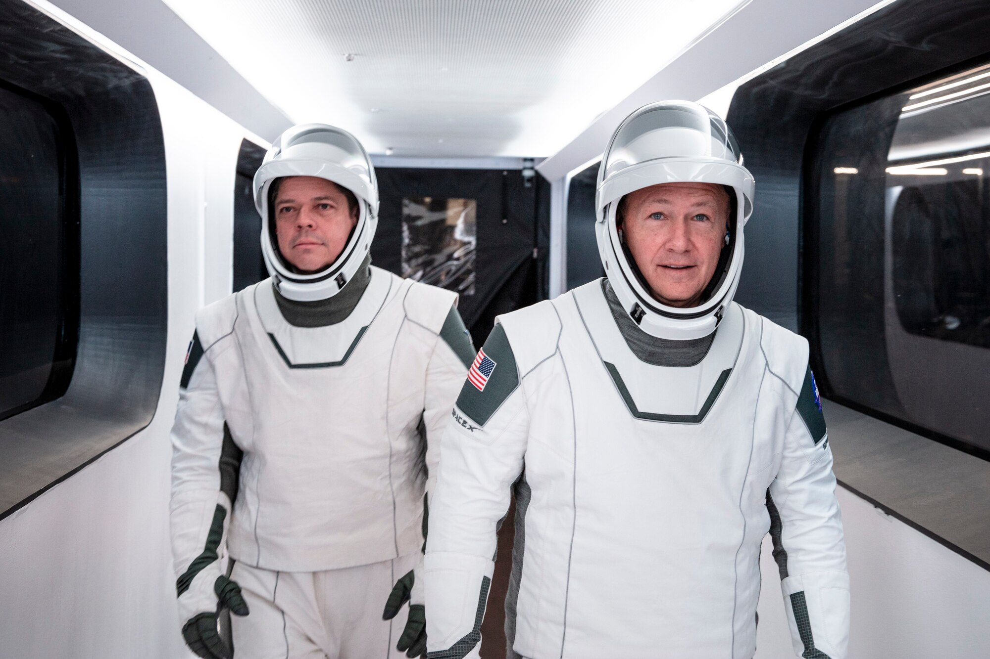 NASA astronauts Bob Behnken, left, and Doug Hurley, wearing SpaceX spacesuits, walk through the Crew Access Arm connecting the launch tower to the SpaceX Crew Dragon spacecraft during a dress rehearsal at NASA’s Kennedy Space Center in Florida on Jan. 17, 2020. A SpaceX Falcon 9 rocket and Crew Dragon spacecraft stand on the launch pad at Launch Complex 39A ahead of the company’s uncrewed In-Flight Abort Test. The flight test will demonstrate the spacecraft’s escape capabilities in preparation for crewed flights to the International Space Station as part of the agency’s Commercial Crew Program. Behnken and Hurley are slated to fly on the company’s first crewed mission, Demo-2.