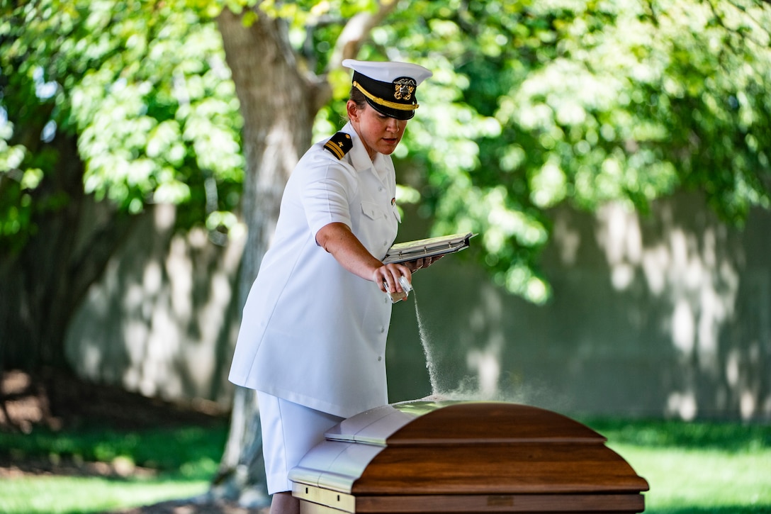 A Navy officer stands over a coffin while holding a notebook.