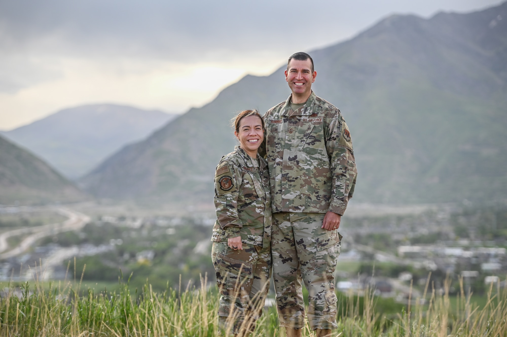 A military couple poses with mountains in the background.