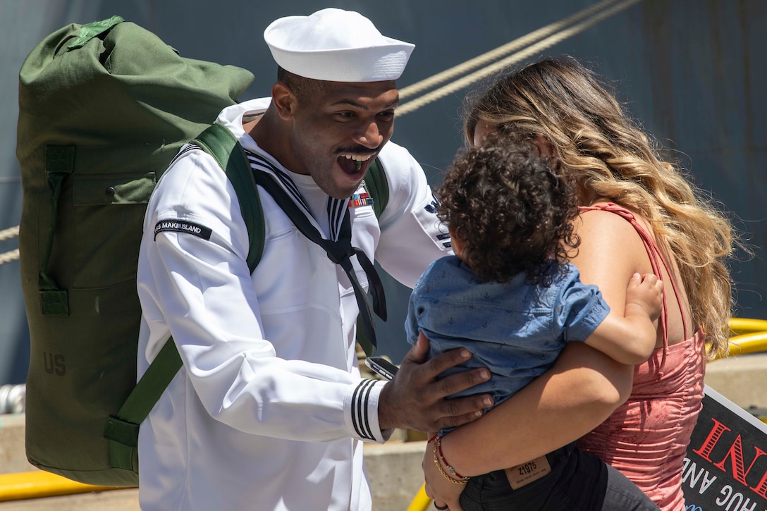 A sailor smiles broadly as he greets his family.