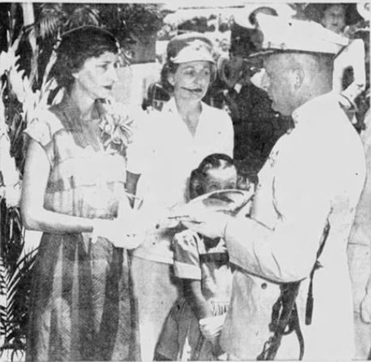 A woman looks at a man presenting her with something. Another woman and a girl stand beside them.