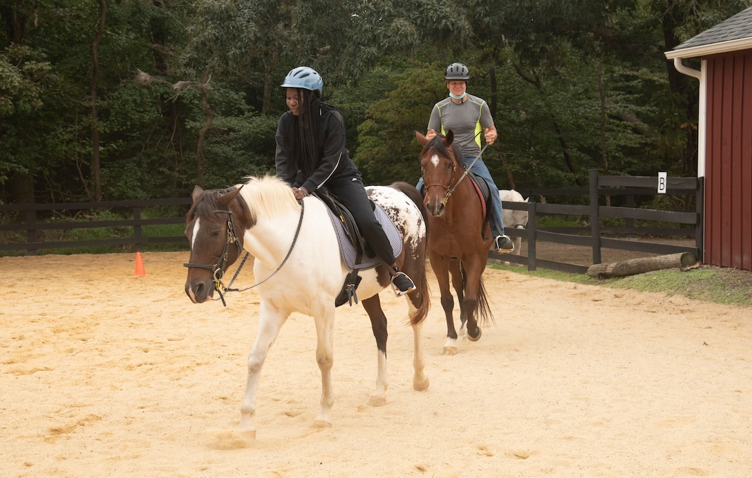 Service members ride horses in fenced-in pen.