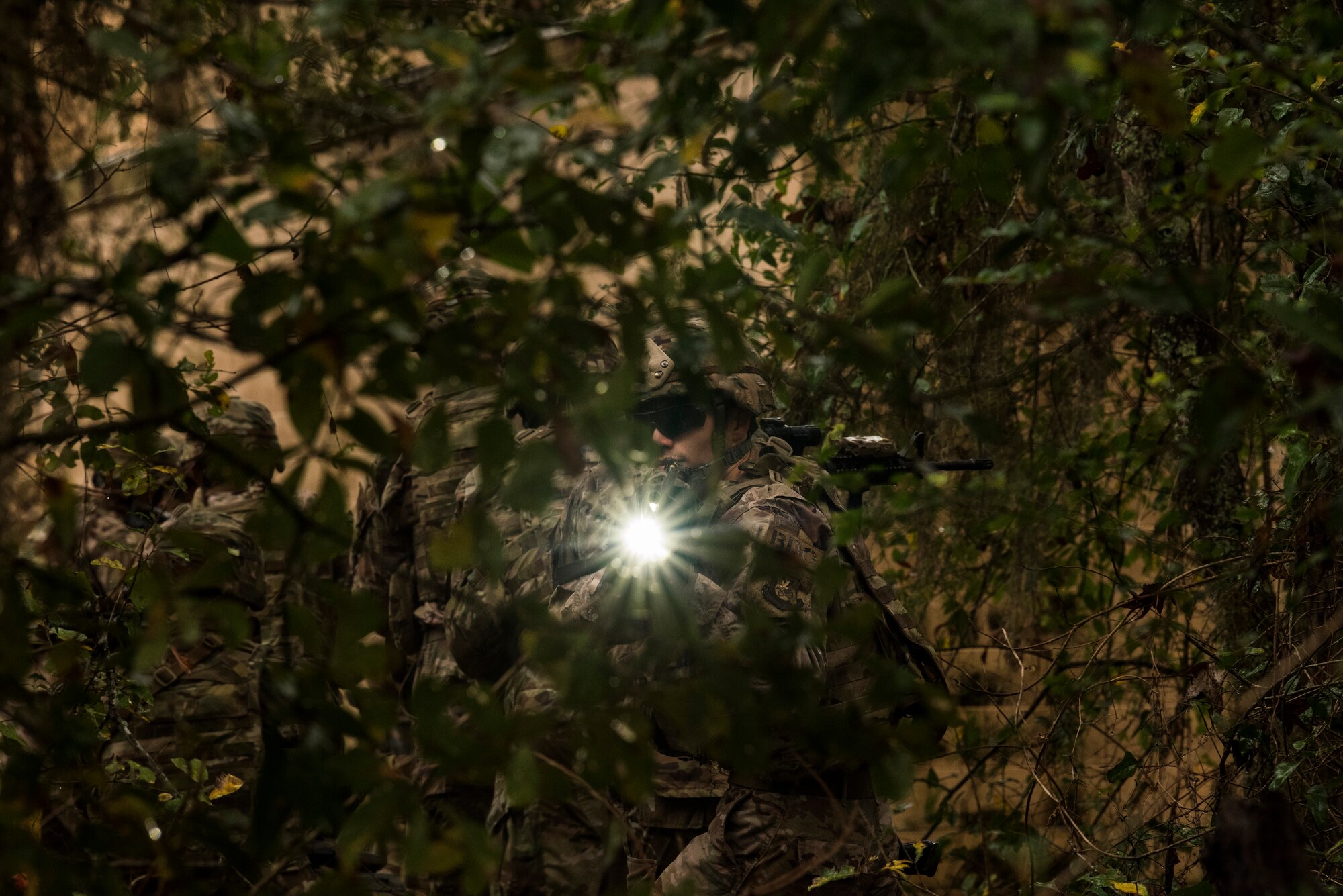 A member of the 823rd Base Defense Squadron shines a light, mounted to an M4 carbine, while tactically moving through dense brush during a training scenario, Moody Air Force Base, Jan. 12, 2018. The 823rd is one of three operational security forces squadrons under the 820th Base Defense Group whose mission is to provide high-risk force protection and integrated base defense for expeditionary forces. (U.S. Air Force photo by Bennie J. Davis III)