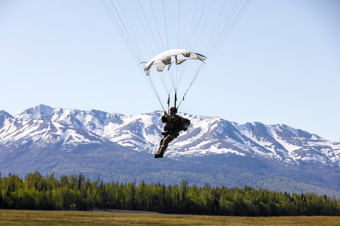 A soldier wearing a parachute descends in the sky; a mountain can be seen in the background.