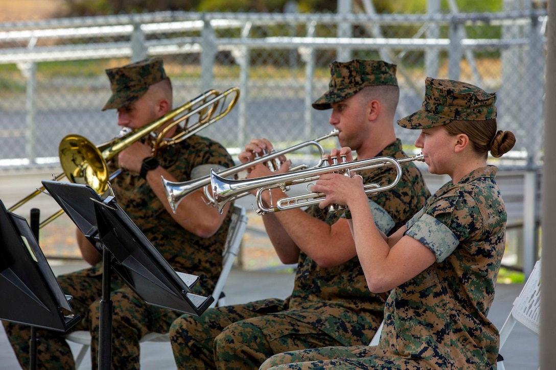 Three Marines sit on chairs playing instruments.