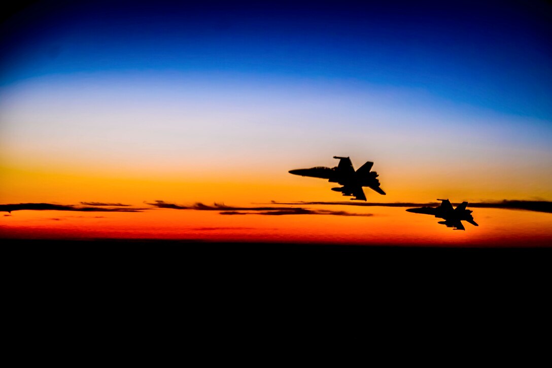 Two aircraft shown in silhouette fly in the sky.