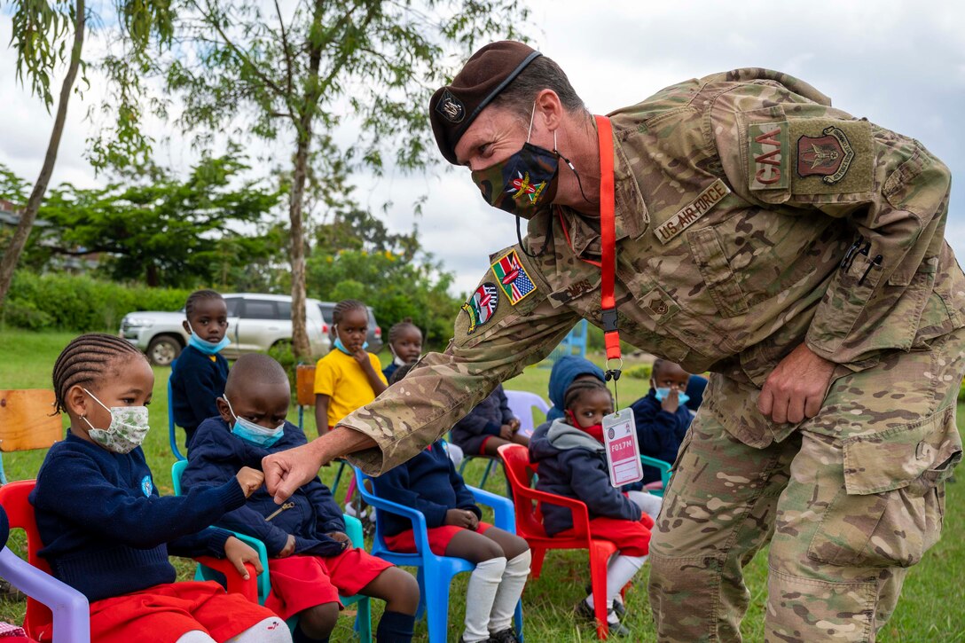 An airman fist bumps a child as other children sit beside.