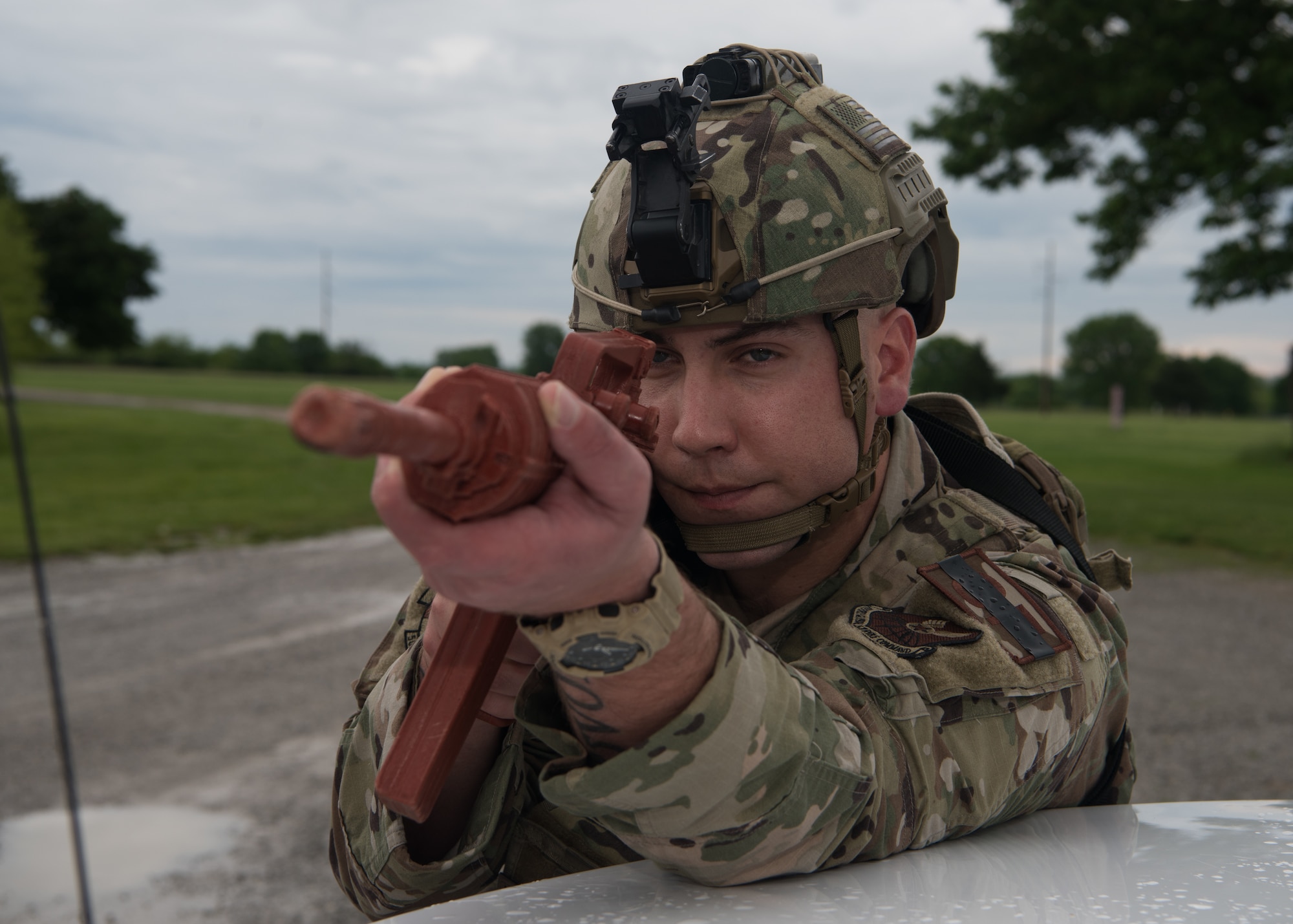 a 509th Security Forces Squadron Airman aims a training rifle while bracing against a police car.