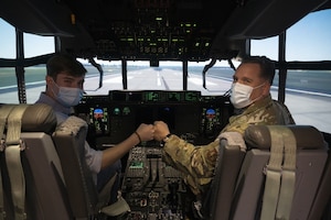 U.S. Air Force Master Sgt. Daniel Williams, 435th Contingency Response Support Squadron air advisor operations superintendent, right, and his son, Ethan Williams, fist bump in a C-130J aircraft simulator at Ramstein Air Base, Germany, May 17, 2021. Ethan enlisted in the Air Force just before his father plans to retire, adding to his family’s legacy of service. (U.S. Air Force photo by Senior Airman Taylor Slater)