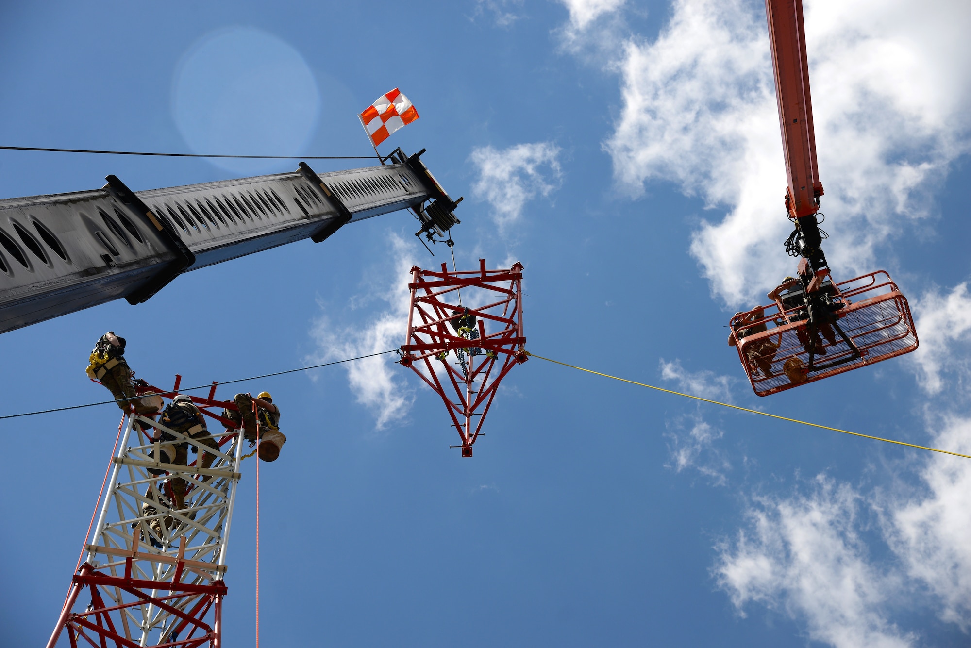 An image of Airmen with the Massachusetts and Pennsylvania Air National Guard working in unison as they use climbing gear to secure themselves safely to a tower, operate a high lift for inspection purposes and use a mobile crane to hoist and connect the top section of a radio communications tower.