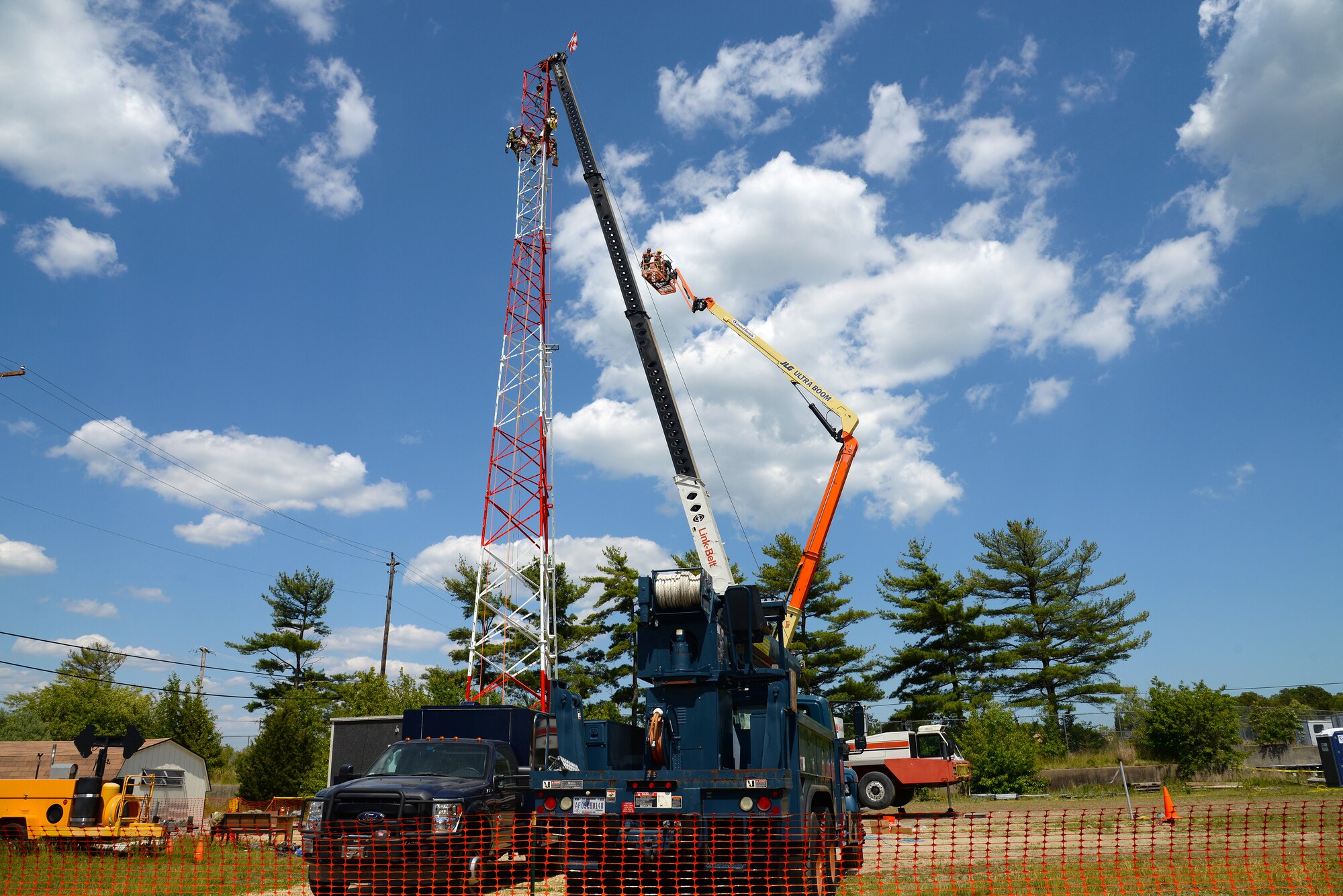 An image of Airmen with the Massachusetts and Pennsylvania Air National Guard working in unison, using climbing gear to secure themselves safely to a tower, operating a high lift for inspection purposes and using a mobile crane to hoist and connect the top section of a radio communications tower.