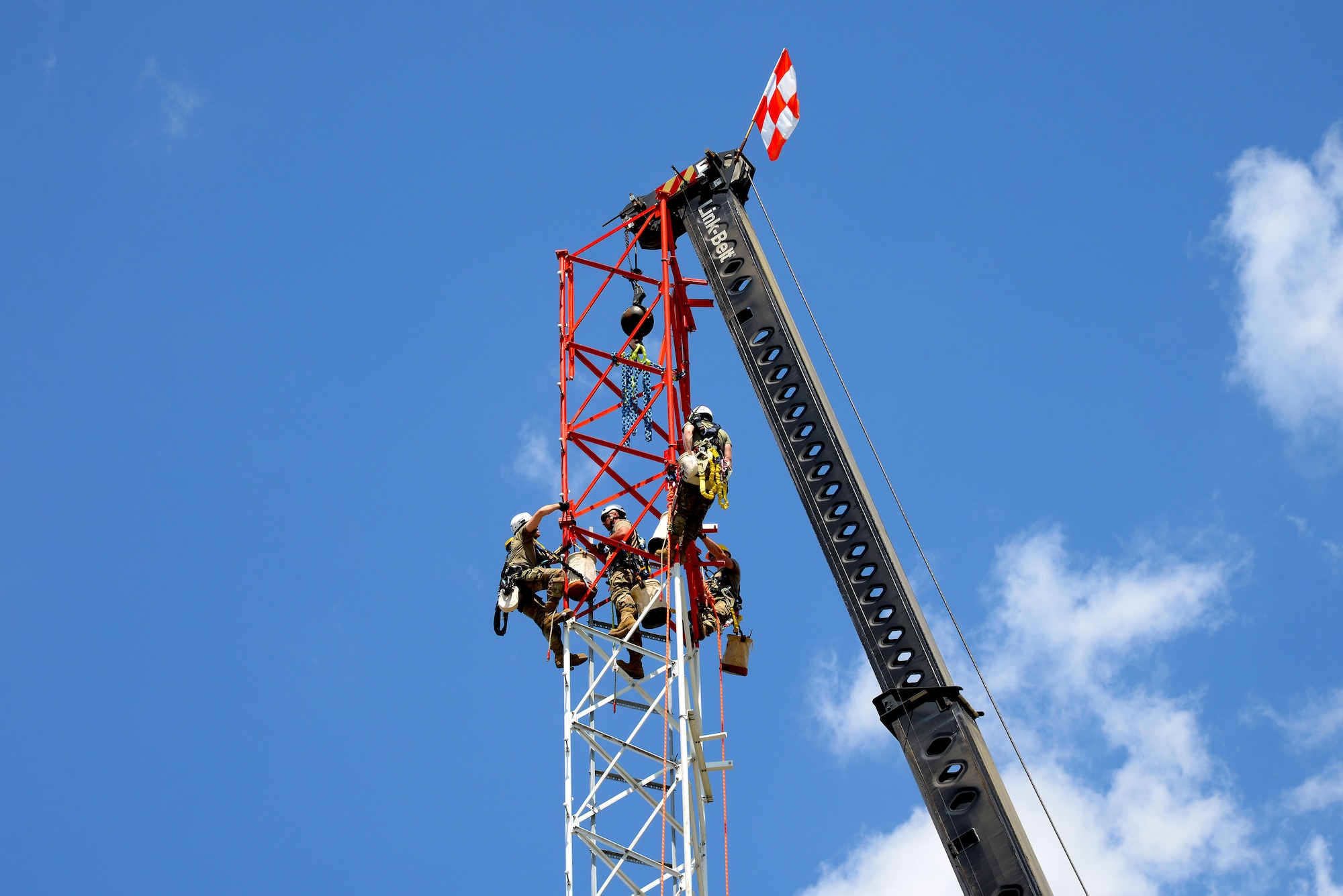 An image of Airmen with the Massachusetts and Pennsylvania Air National Guard connecting the top section of a radio communications tower being hoisted by mobile crane.