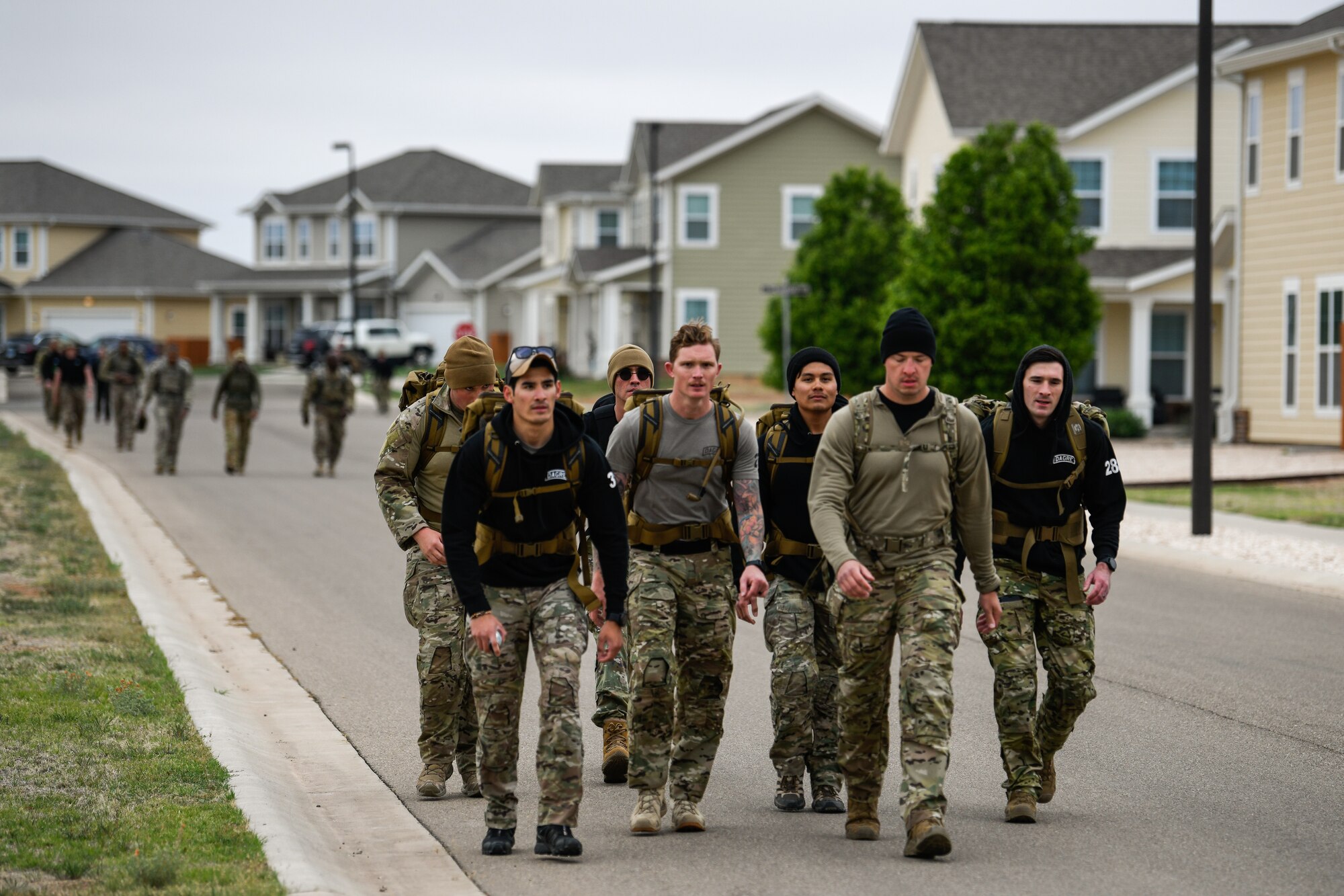 A group of Airmen marches through a suburban style neighborhood with heavy backpacks.