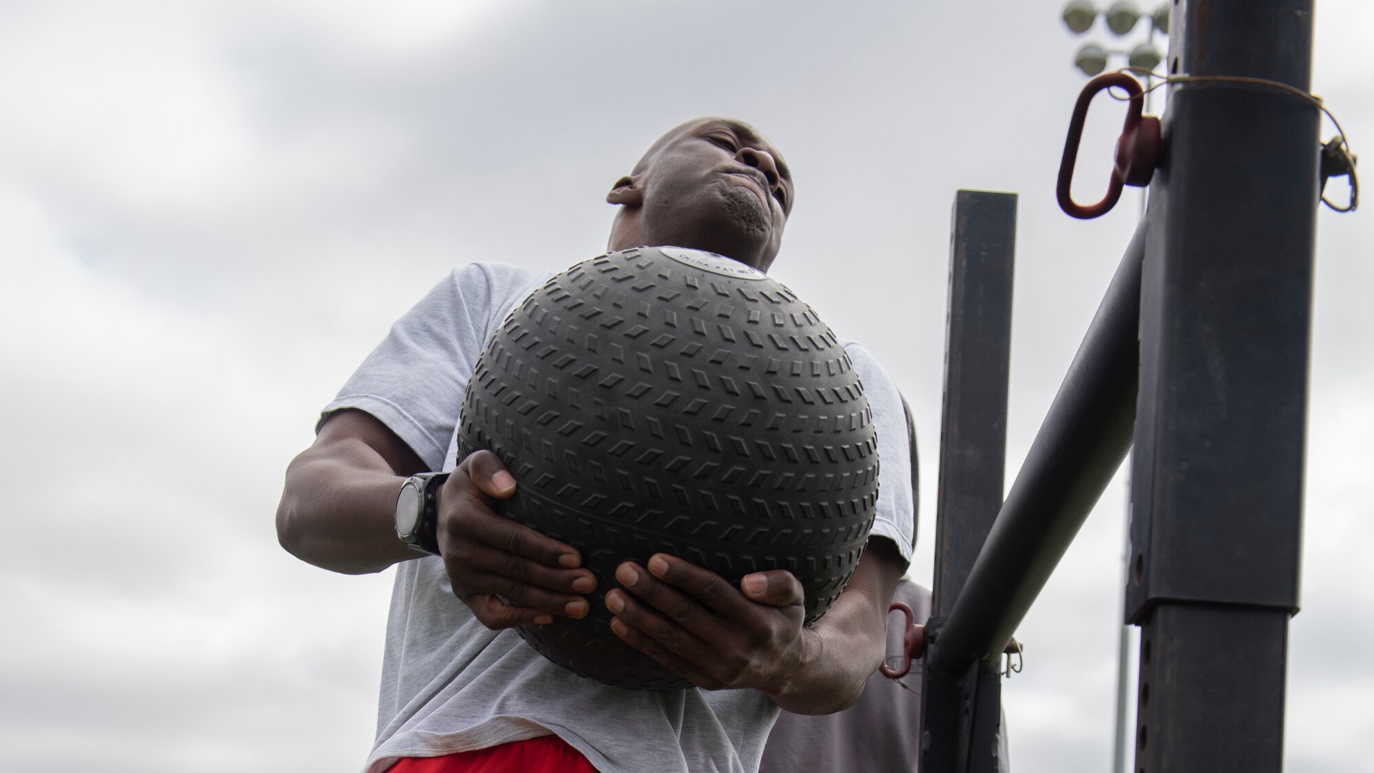 A man strains as he lifts a heavy medicine ball over a raised bar.