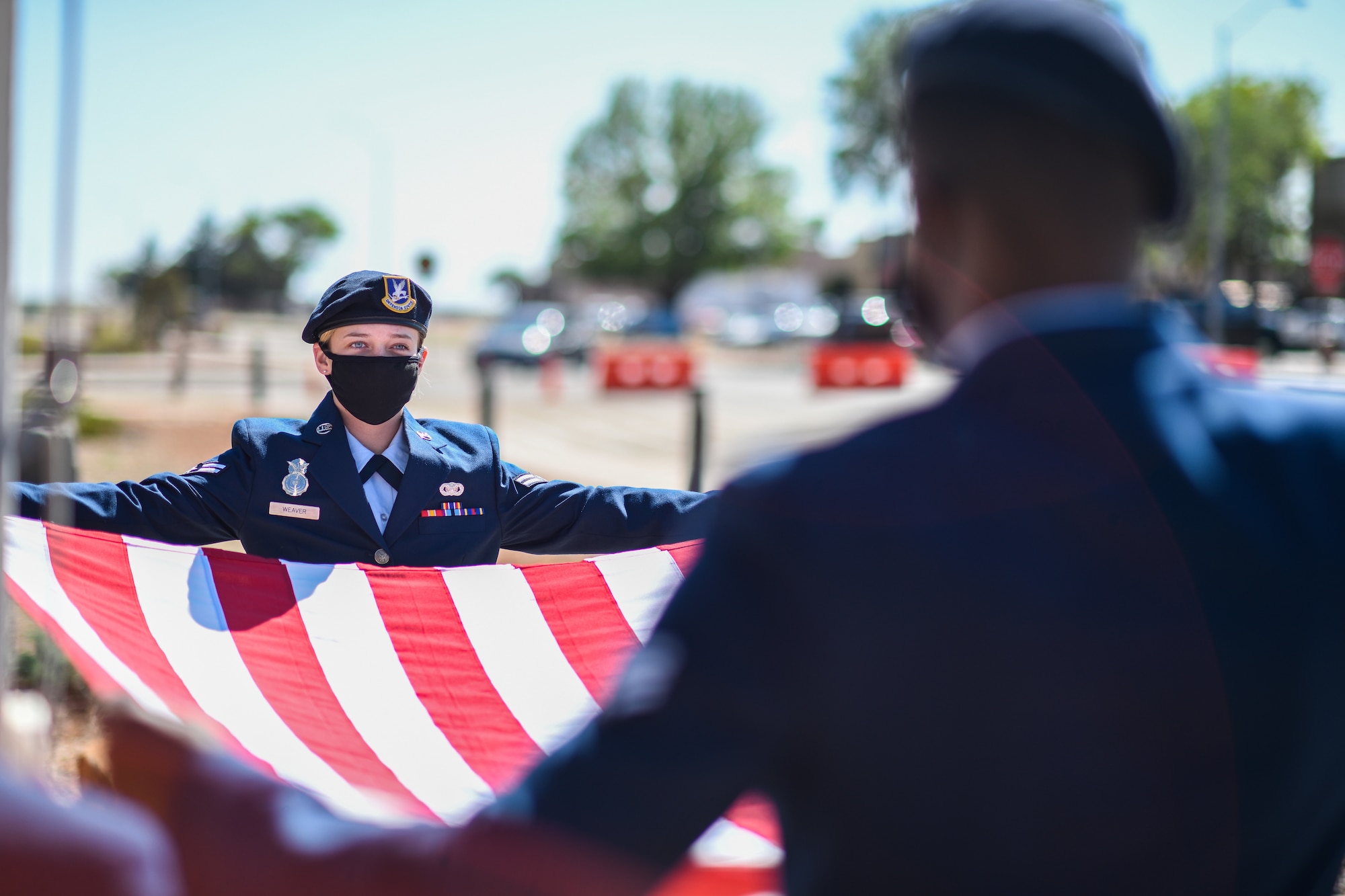 Two Security Forces Airmen in their dress blues uniform hold a flag open as they stand at the position of attention.