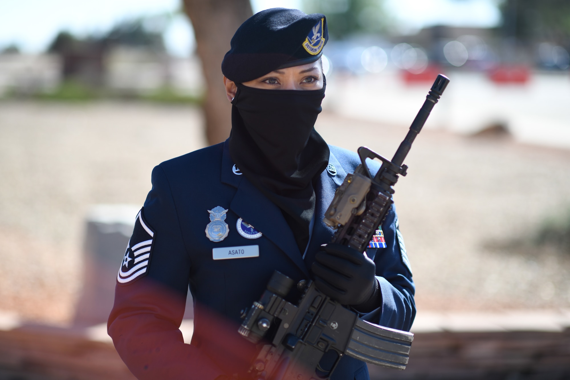 A Security Forces Master Sergeant in her dress blues uniform stands at attention and holds an M4 rifle in the 'port-arms' position.
