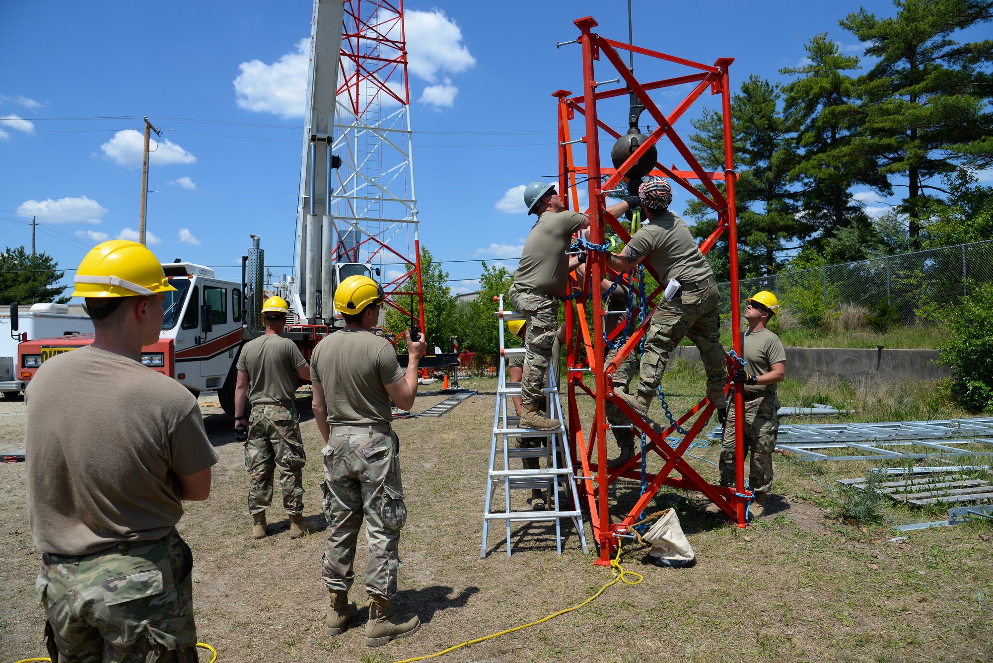An image of Airmen with the Massachusetts and Pennsylvania Air National Guard attaching lifting straps to the top section of a radio communications tower.