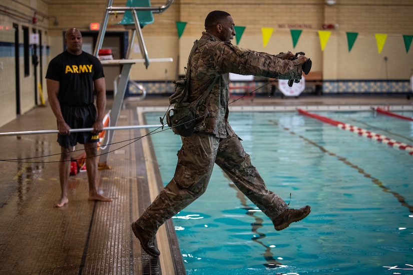 A male soldier crawls through an obstacle course.