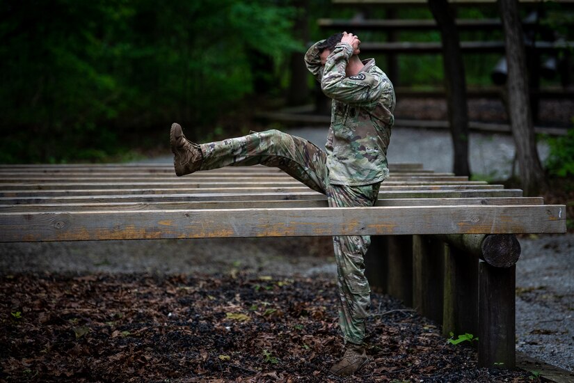 A male soldier crawls through an obstacle course.