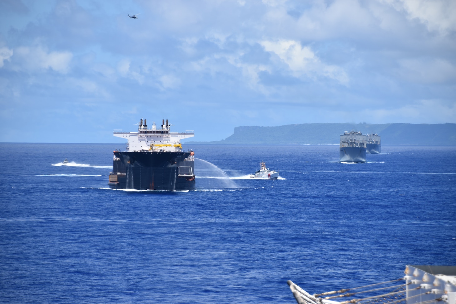 While steaming in a formation near Guam, USNS Montford Point employs their hose, a pre-planned response, which it might use during convoy operations.  Pictured from left are:  a Coastal Riverine Group 1’s mark VI boat, USNS Montford Point (T-ESD 1), U.S. Coast Guard Cutter Myrtle Hazard (WPC-1139), USNS Red Cloud (T-AKR 313), USNS Watkins (T-AKR 315), and in the air, an MH-60R from Helicopter Sea Combat Squadron 25.