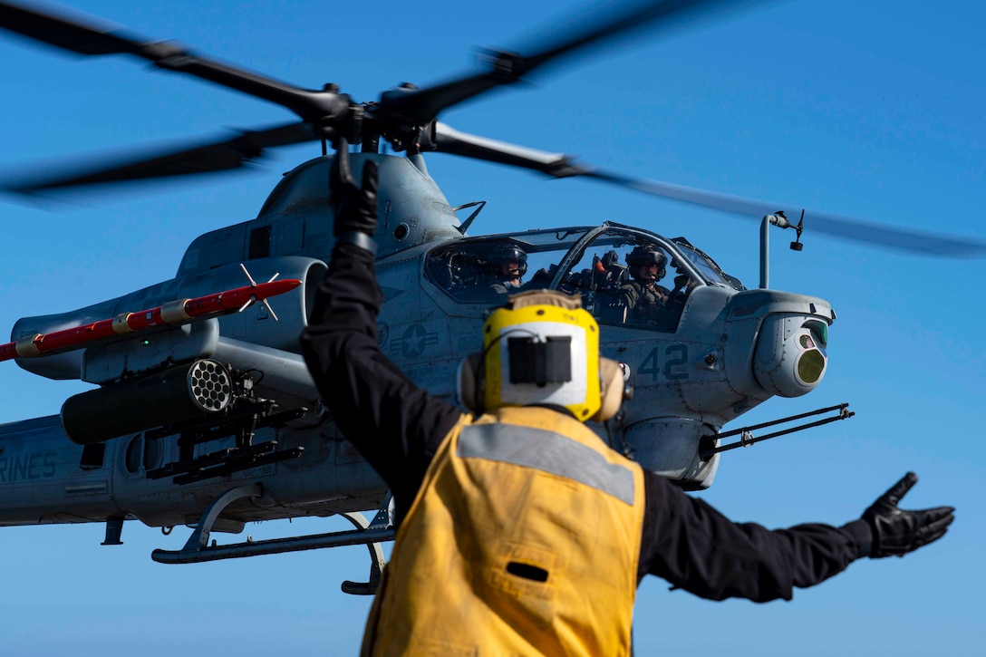 A sailor signals toward an airborne helicopter.