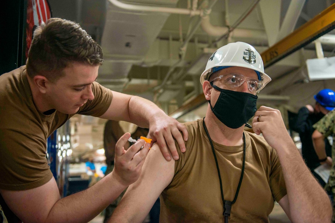 A sailor injects another sailor in the arm with a needle.