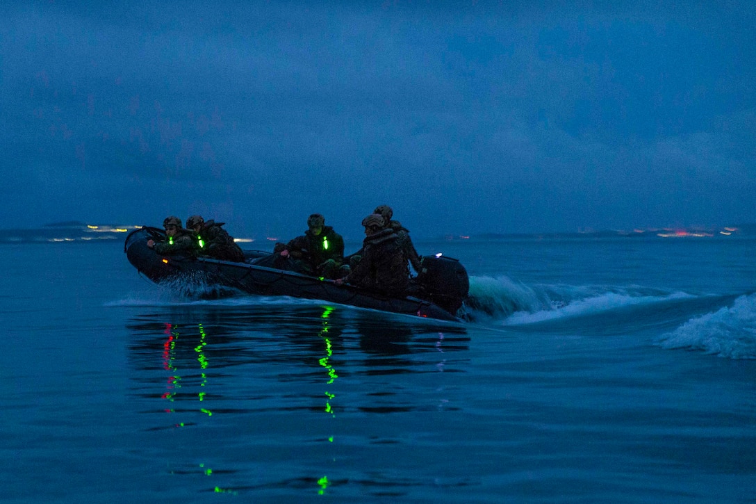 Marines travel in a combat rubber raiding craft through waters at a night.