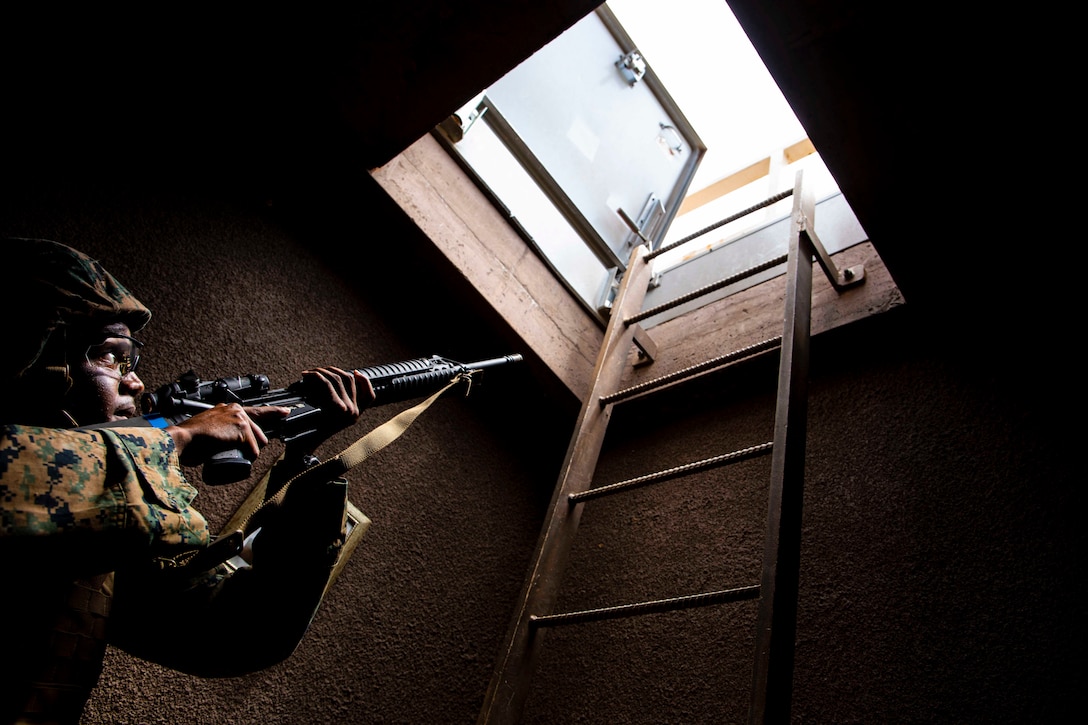 A Marine points a weapon at an open door above him.