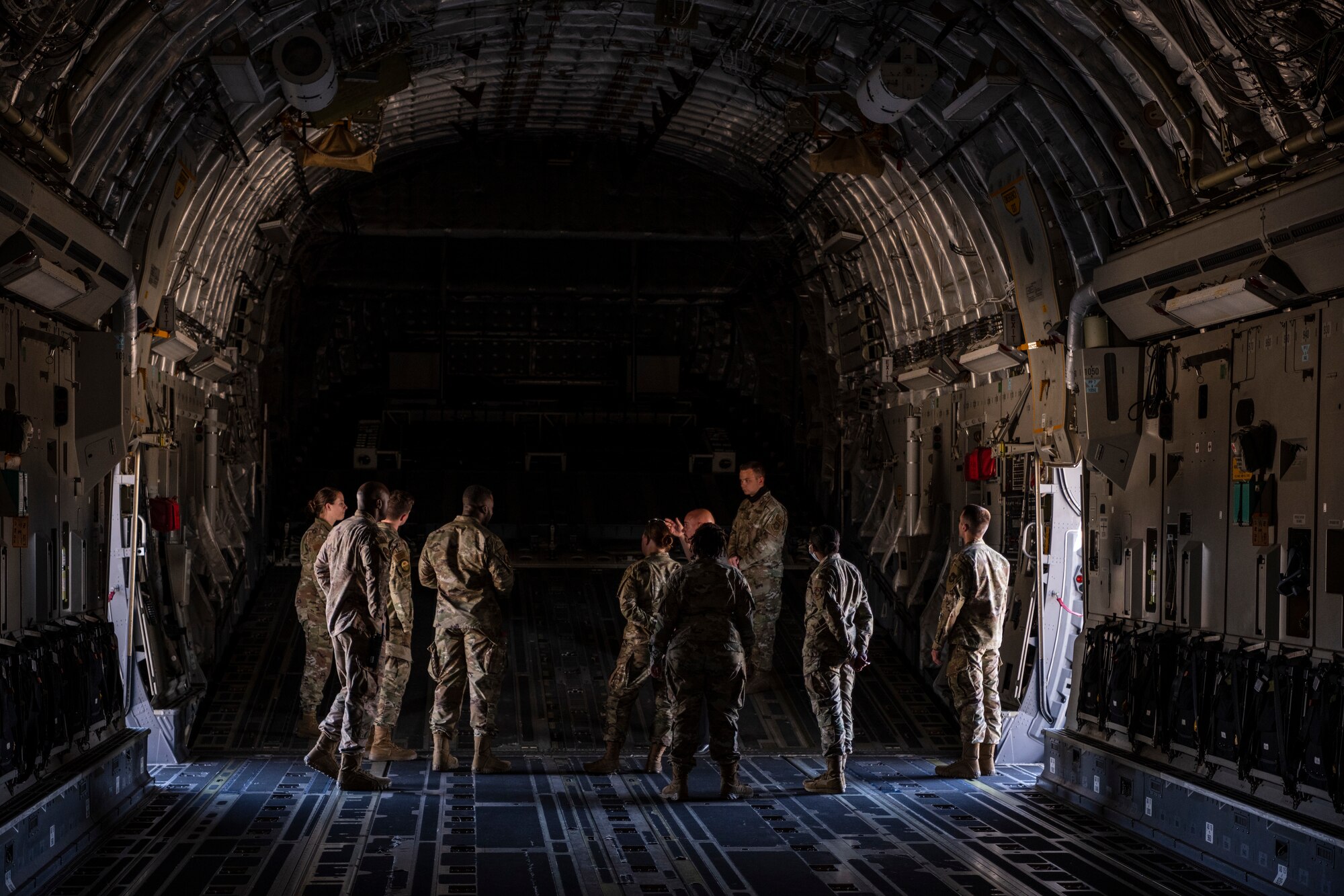 A group of Airmen stand around at the back of a large military aircraft.