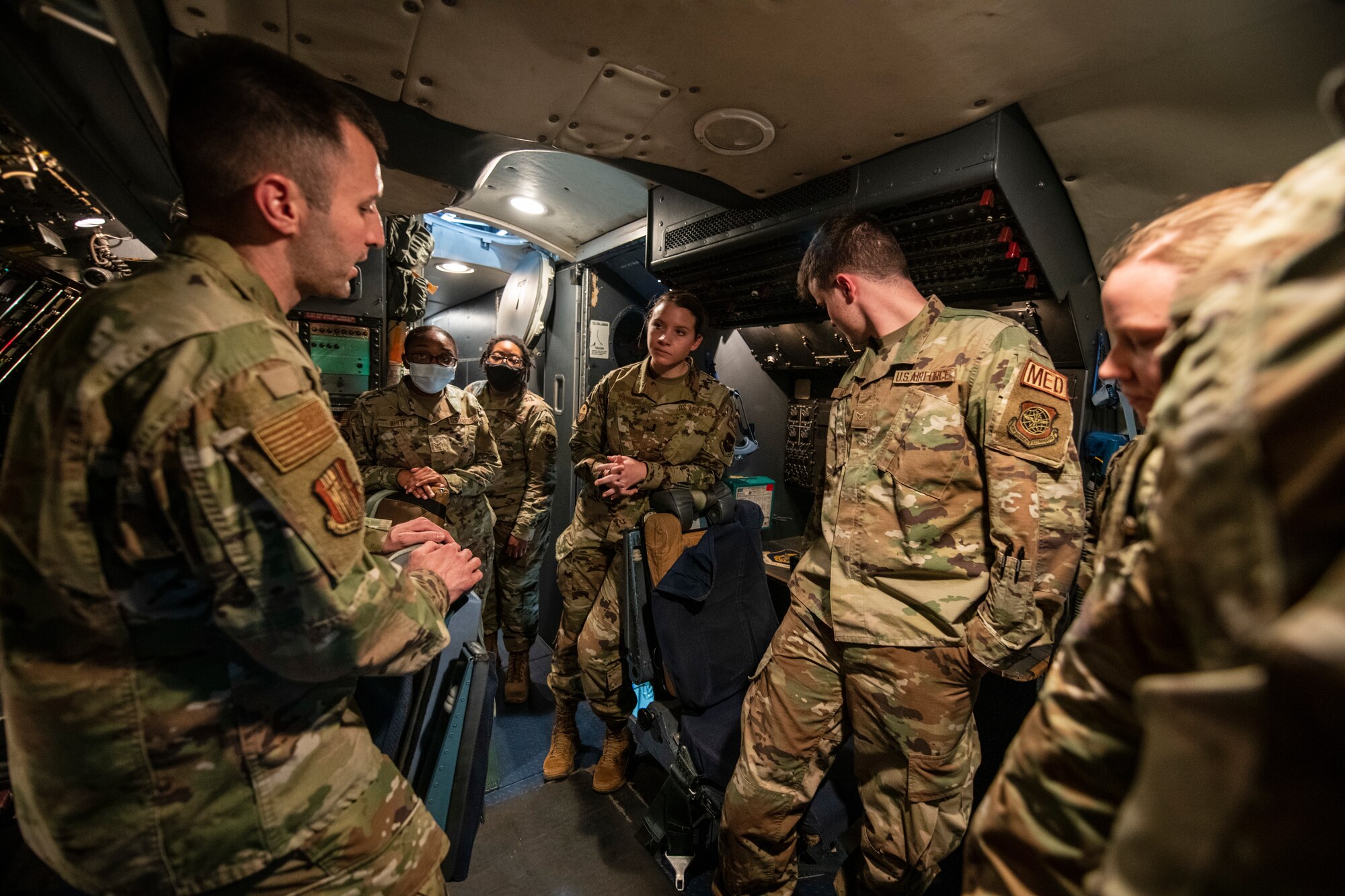 Airmen stand around in a circle inside of a cockpit of a large military aircraft.