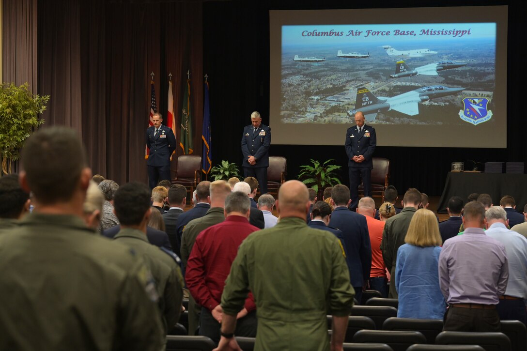 The official party and audience members attending the graduation of Specialized Undergraduate Pilot Training class 21-10 lower their heads in prayer May 27, 2021, on Columbus Air Force Base, Miss. The 21 graduates completed a 52-week pilot training program including academics, physiological training, and flight training in the T-6A Texan II, T-1A Jayhawk, and T-38C Talon. (U.S. Air Force photo by Senior Airman Jake Jacobsen)
